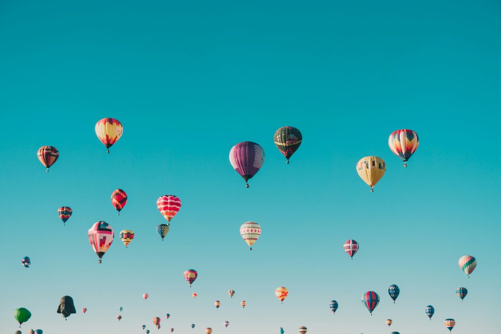 Photo of a clear blue sky with dozens of colorful hot balloons.