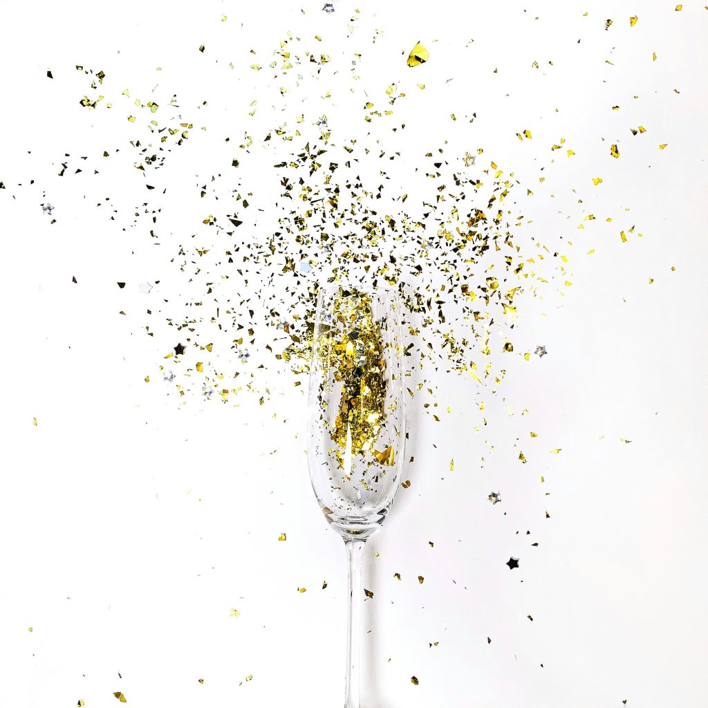 Image of a champagne glass filled with gold glitter that explodes out into the background.