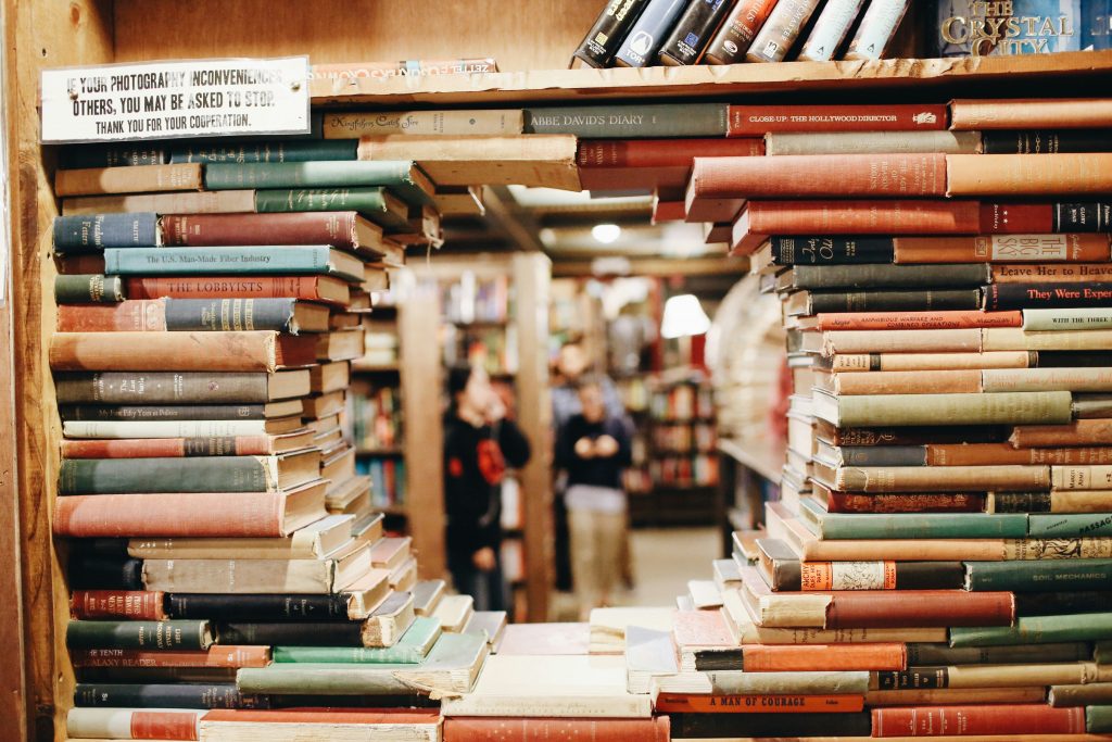 Image shows a "wall" of books arranged with a hole in the middle to see through to a blurry background of readers in a library.