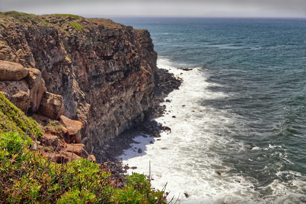 Image shows a rocky cliff line with some grass against a rough sea.