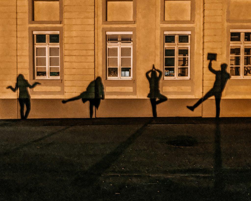 Image shows four shadows of people in movement on a background of a building wall with windows.